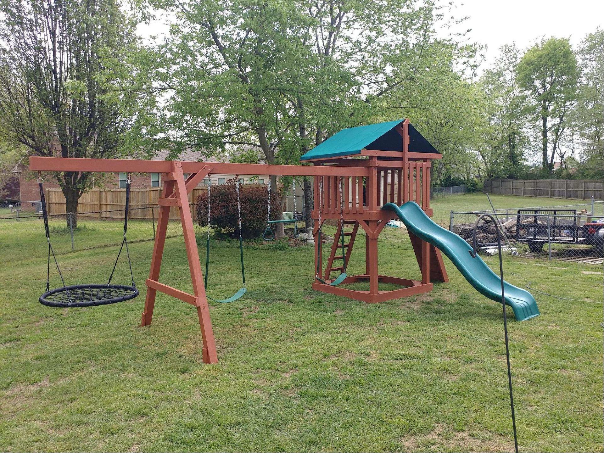 Backyard wooden playset with blue slide, swings, and climbing platform on grass, surrounded by trees