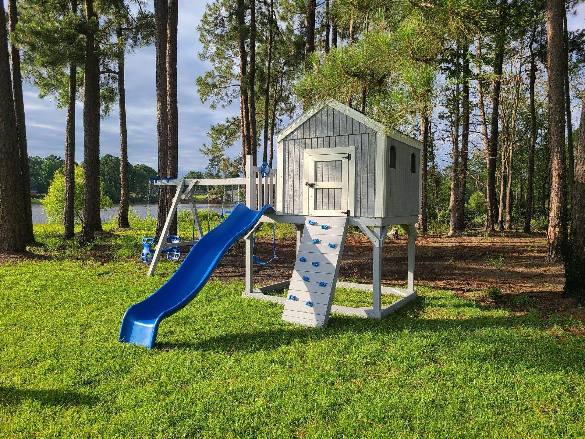 Backyard playhouse with blue slide and climbing wall on a grassy lawn among trees