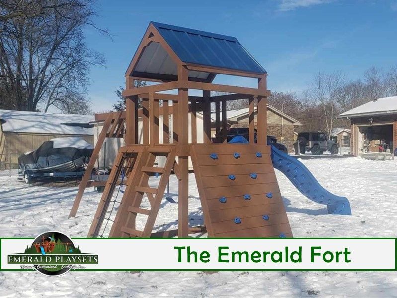 A wooden playground set with a slide and climbing wall is in the snow.