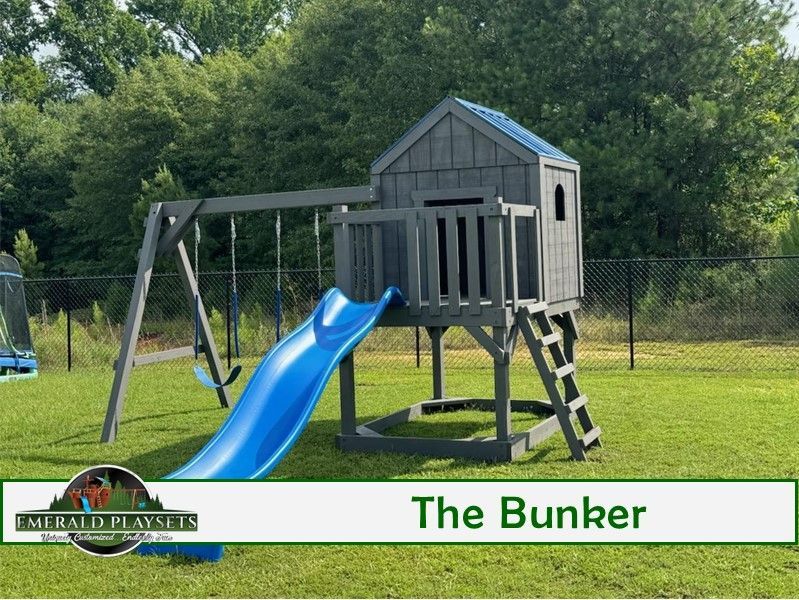 Gray wooden playset with blue slide, swing set, and a small playhouse in a grassy yard.