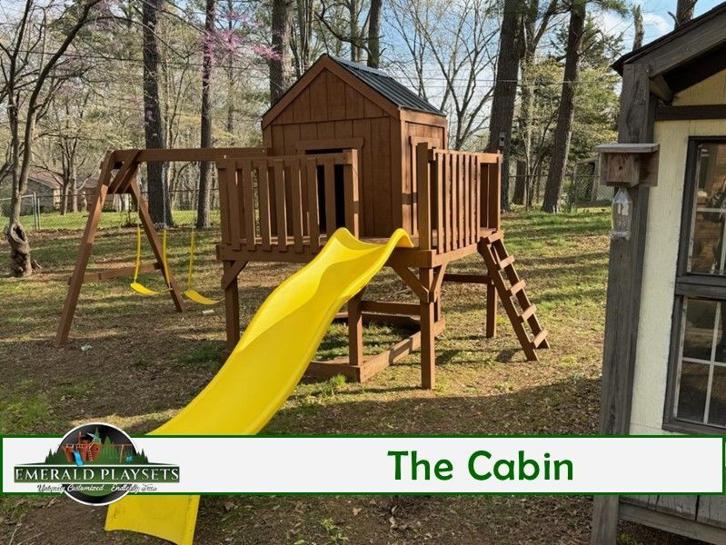 A wooden playground with a yellow slide and a sign that says the cabin