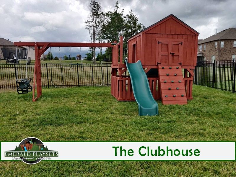 A red playhouse with a green slide and swings in a grassy yard.