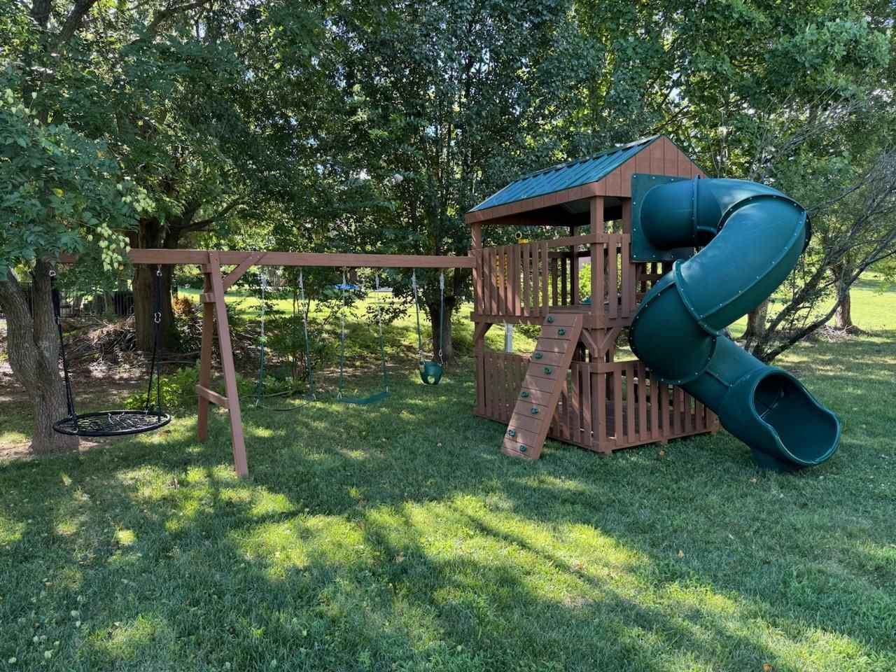 Backyard wooden playset with blue slides and swings on a grassy lawn