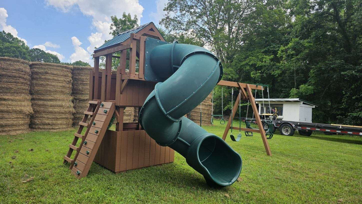 Playground with brown wooden structure, green slide, and swing set in a grassy yard.