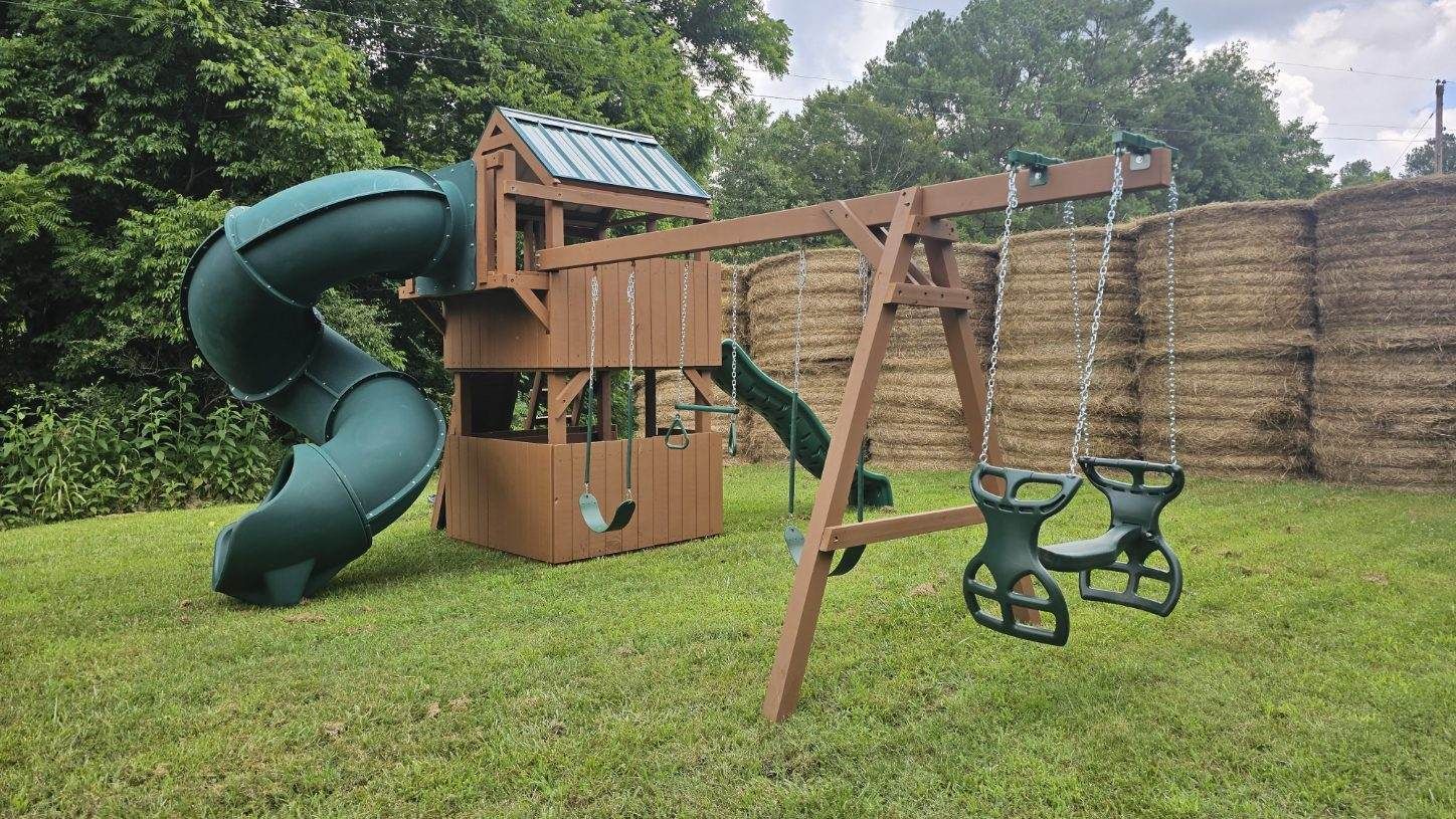 A wooden playground set with a slide and swings in a backyard.