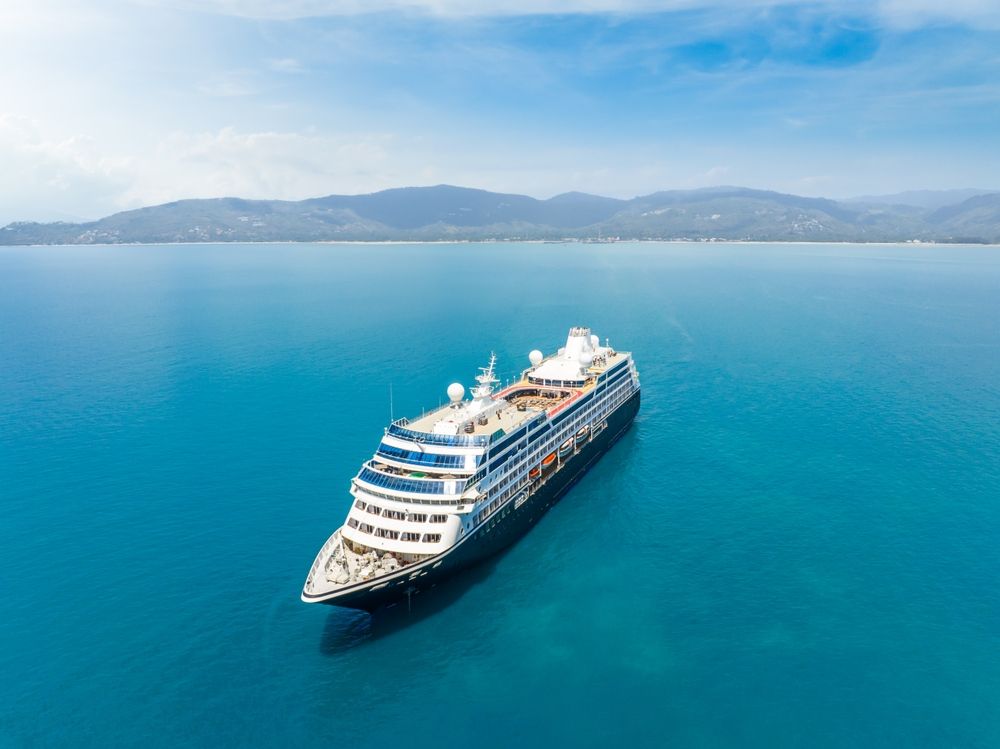 Cruise ship on a turquoise sea, mountains in the background under a blue sky.