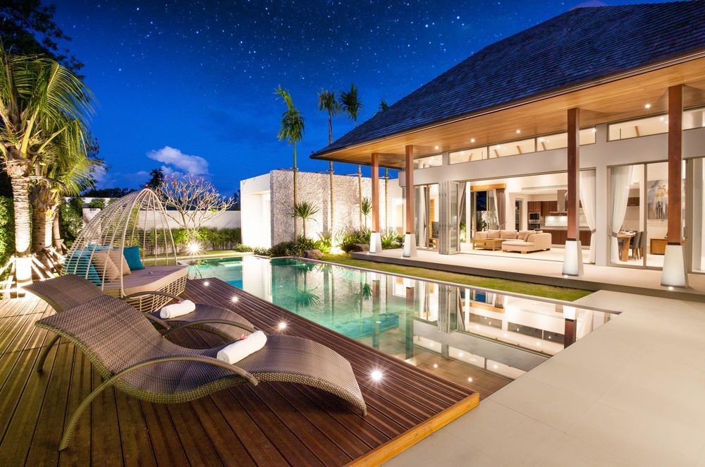Luxury villa with pool at night, wooden deck with lounge chairs, stars visible.