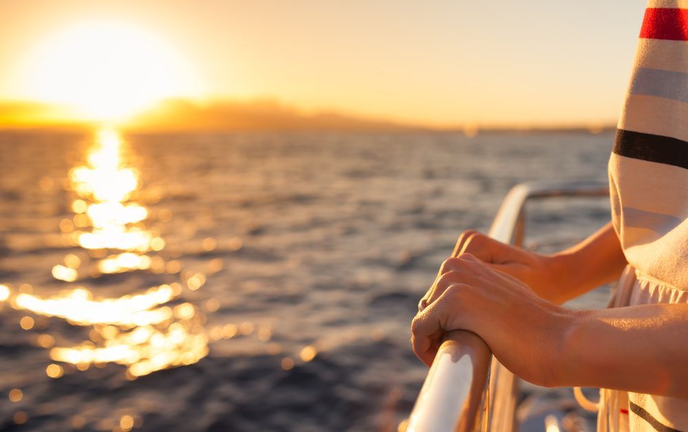 Hands on railing, watching the sunset over the water from a boat.