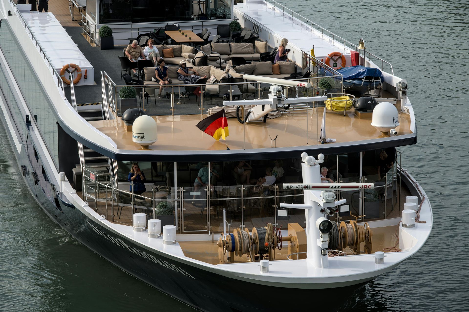 Stern of a large, black and white boat with people lounging on an upper deck. A German flag is visible.