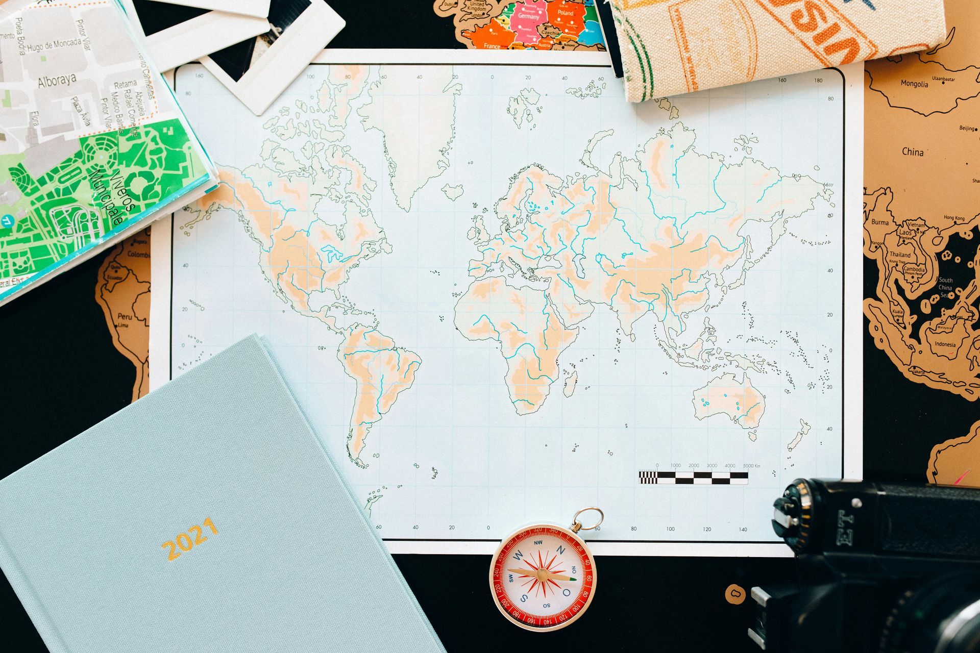 World map with travel items like a compass, camera, passport, and journal, on a dark surface.