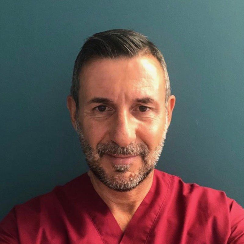 Un professionista con barba e capelli corti e scuri, che indossa una casacca rossa su uno sfondo verde acqua scuro.