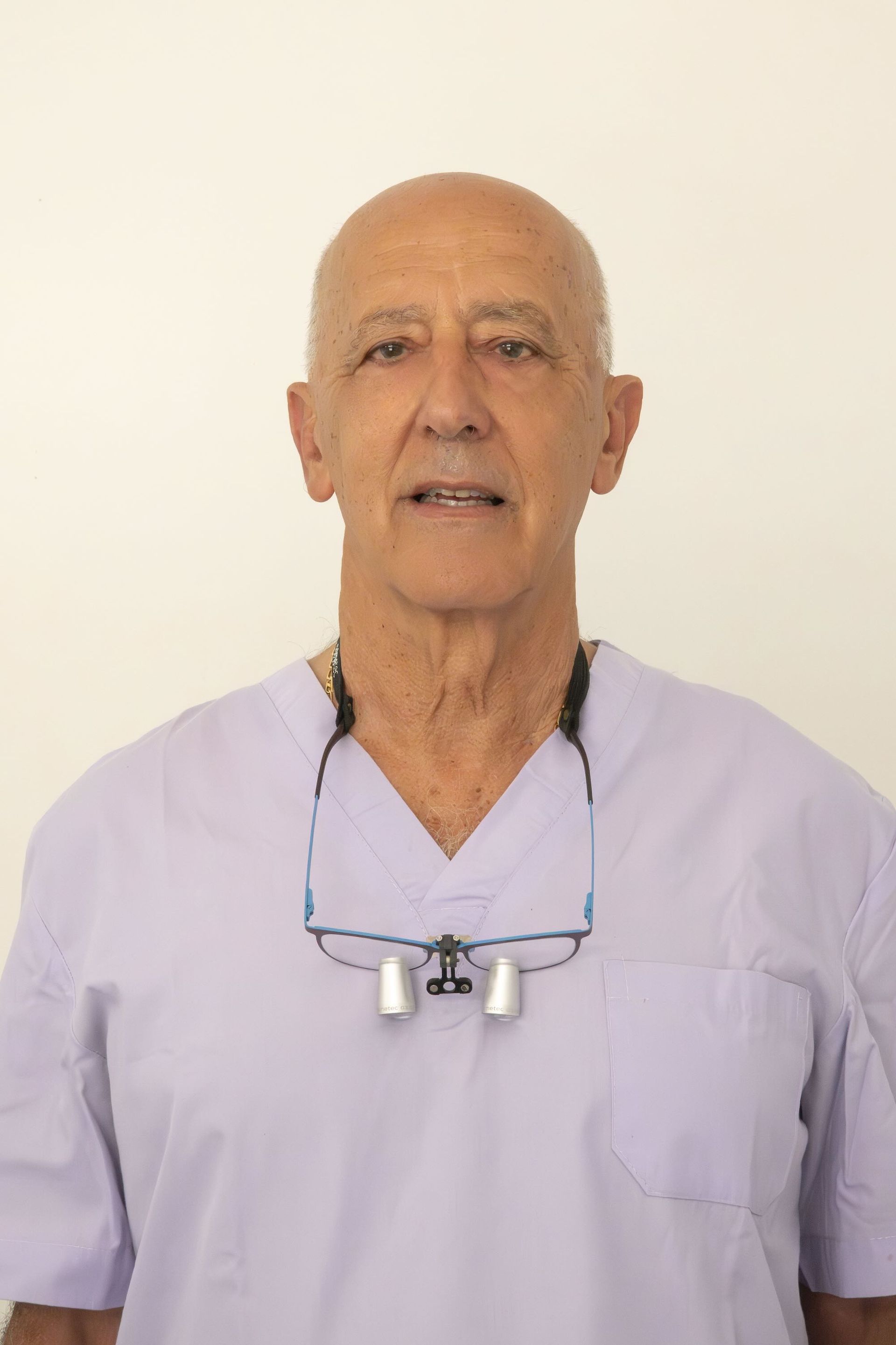 Ritratto ravvicinato di una persona sorridente che indossa una casacca chirurgica azzurra, su uno sfondo rosa sfocato.