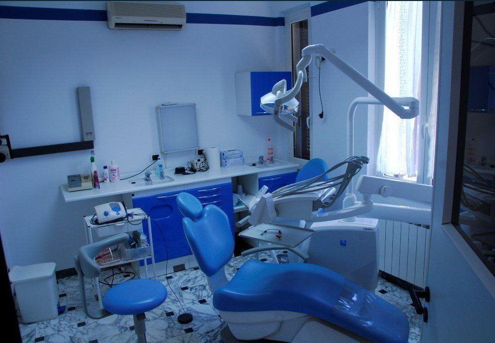 Una sala visite odontoiatriche luminosa e moderna, con poltrona odontoiatrica blu, sgabello abbinato e attrezzature professionali.