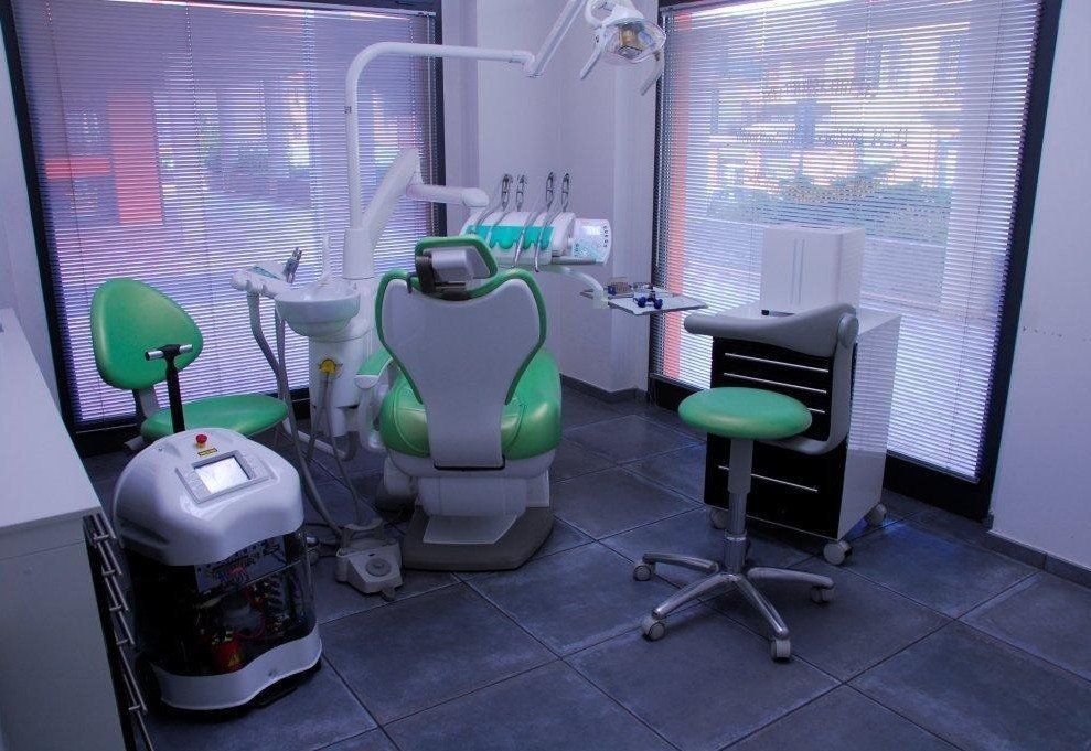 Uno studio dentistico con una poltrona per pazienti di colore verde chiaro, uno sgabello abbinato, attrezzature odontoiatriche e un apparecchio a pavimento.