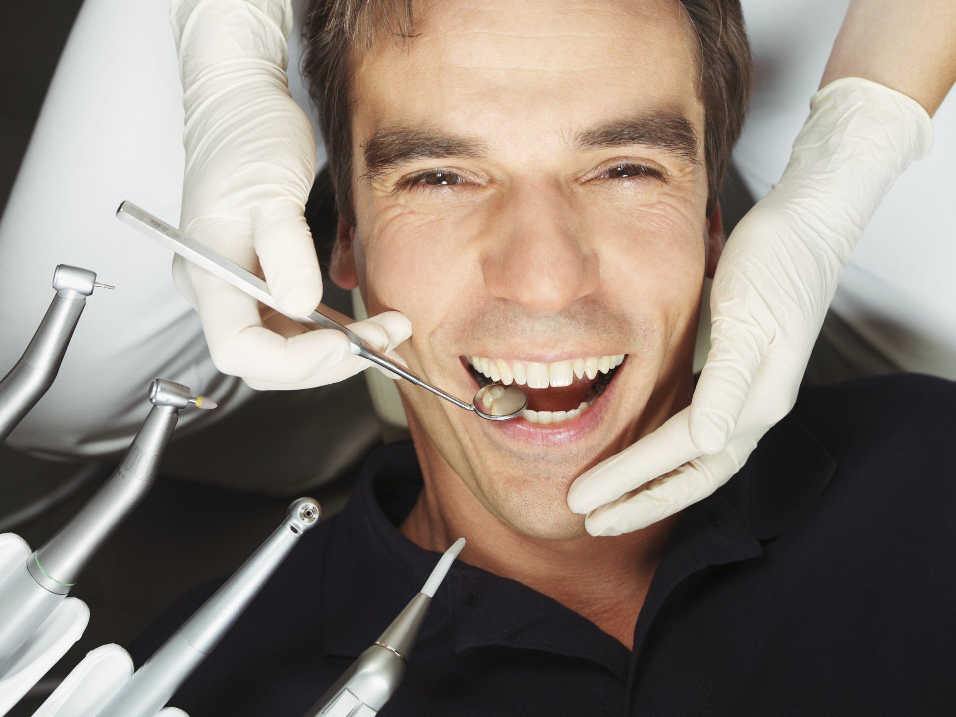 In uno studio dentistico, un dentista con i guanti esamina i denti di un paziente utilizzando uno specchietto.