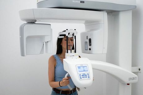 Una persona in piedi in uno studio medico, posizionata all'interno di un apparecchio radiografico digitale panoramico per una scansione dentale.