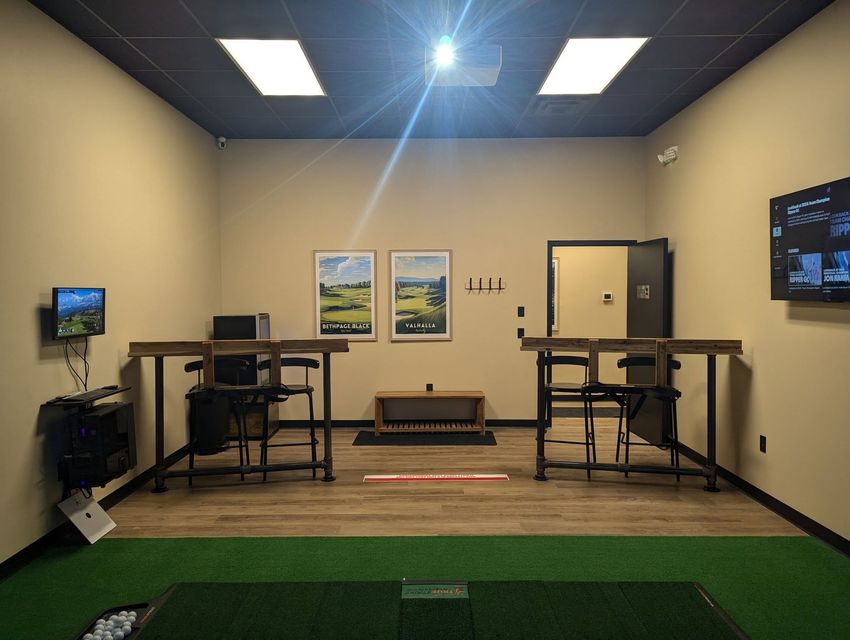 Interior of golf simulator room with two tables, golf mats, and monitors.
