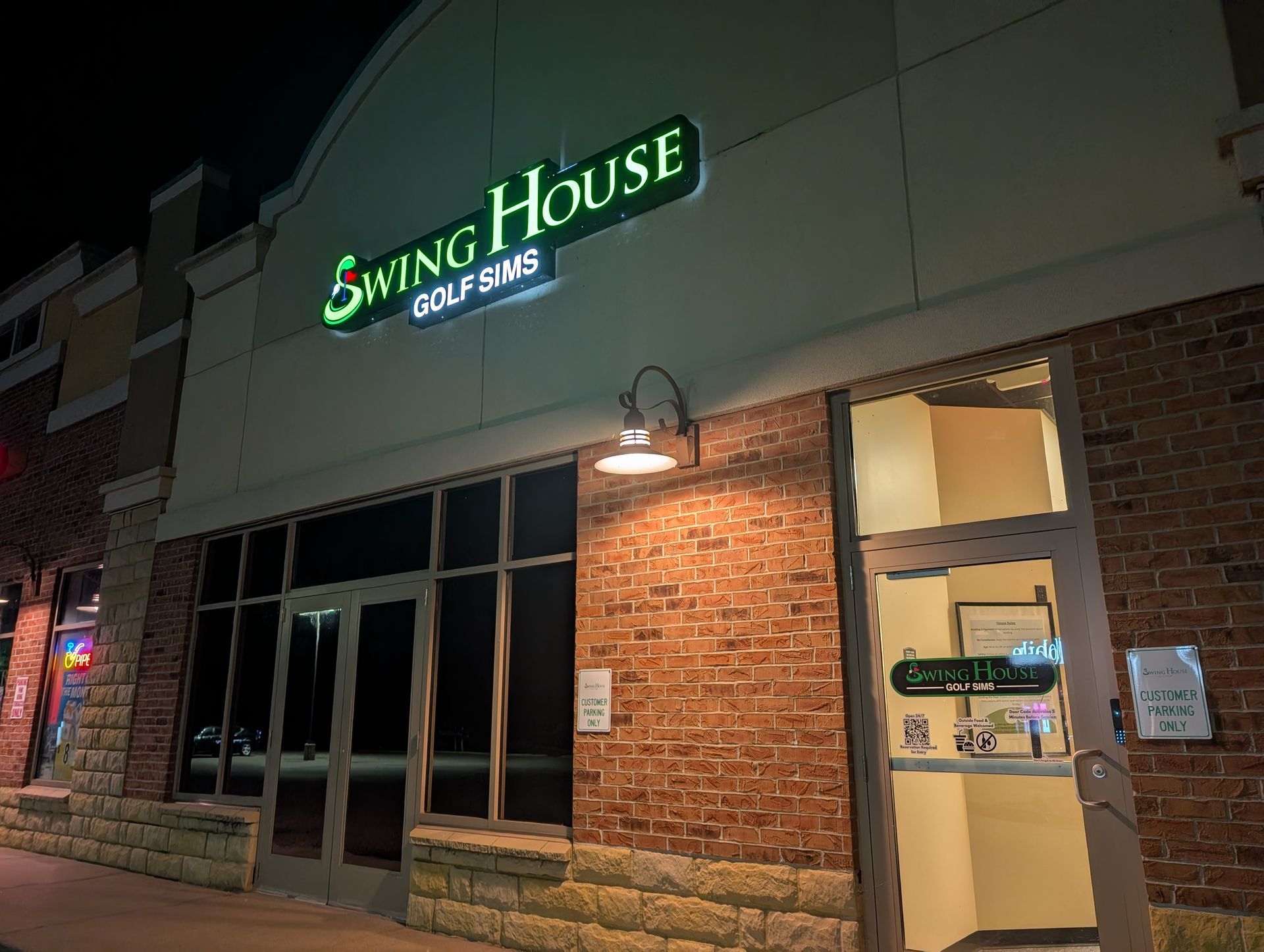 Swing House golf simulators business exterior at night; illuminated sign, brick facade.