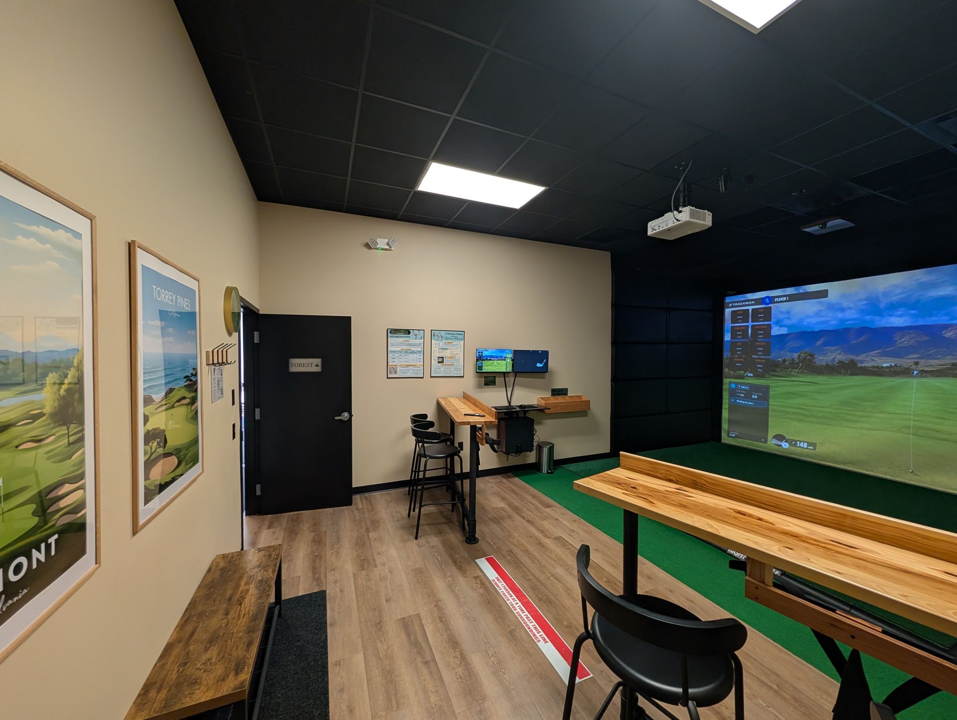 Golf simulator room with a screen displaying a golf course, tables, and chairs.