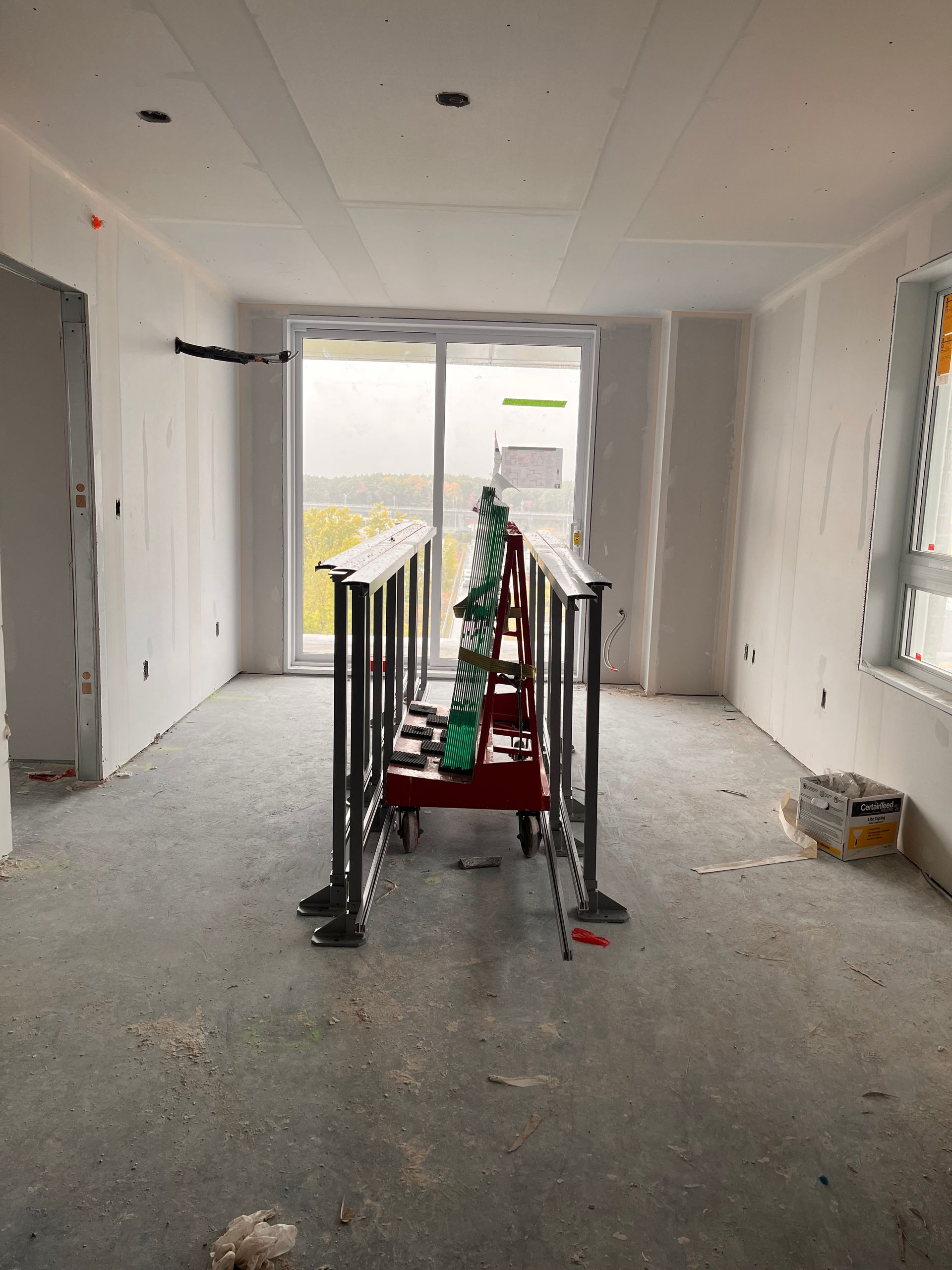 Intérieur d'un chantier : pièce aux murs inachevés, échafaudage de chantier et porte coulissante en verre.