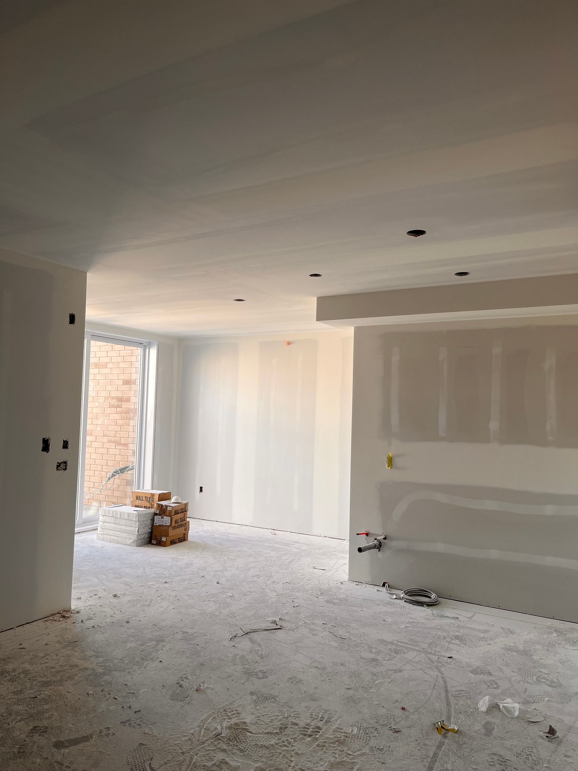 Intérieur d'une pièce en construction, avec des cloisons sèches, des murs et un plafond non finis, et des débris éparpillés.