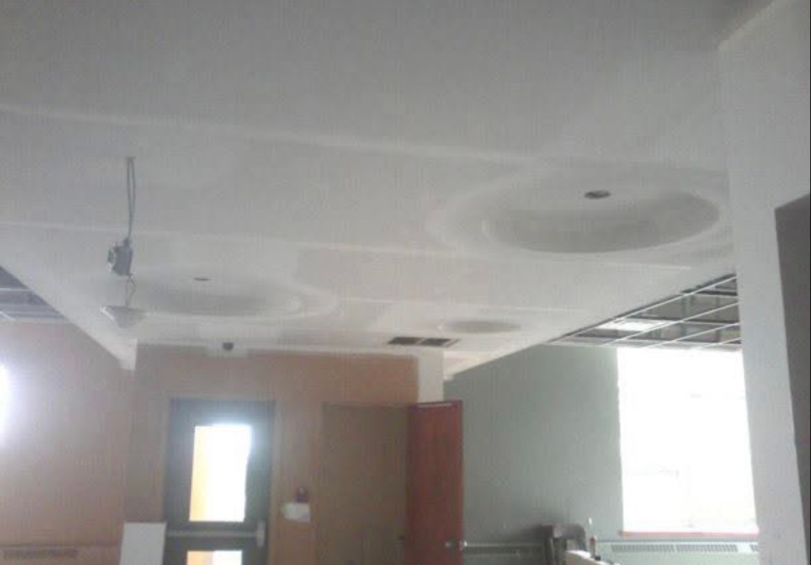 Vue intérieure d'un chantier : plafond inachevé avec inserts circulaires, luminaires et murs partiellement ossature.