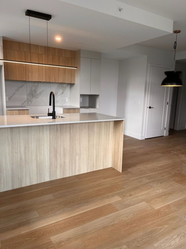 Cuisine moderne avec placards en bois clair, plans de travail blancs et parquet.