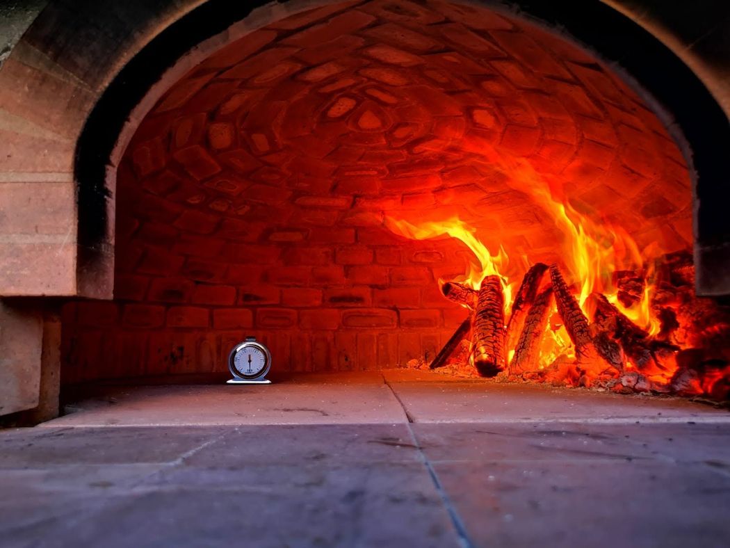 Forno in pietra con fiamme arancioni brillanti che ardono all'interno e un piccolo orologio sul pavimento lì vicino.