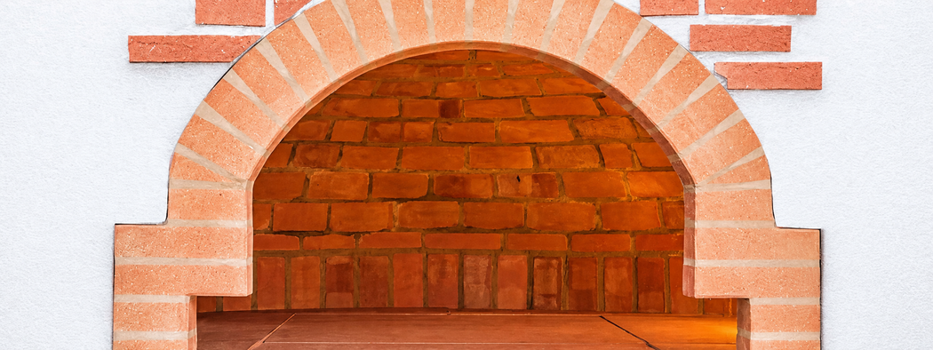 Camino decorativo in mattoni con apertura ad arco e piastrelle in terracotta.