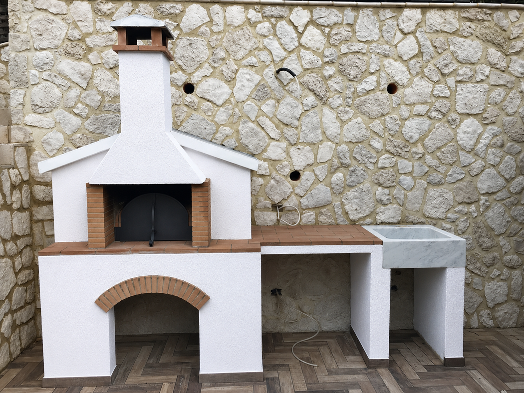 Forno per pizza esterno in mattoni bianchi con camino e legnaia, incassato in un muro di pietra.