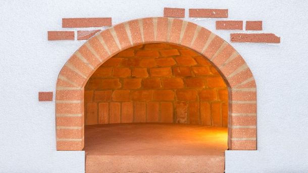 Nicchia in mattoni con forno, apertura ad arco e luce calda all'interno, incassata in una parete bianca.