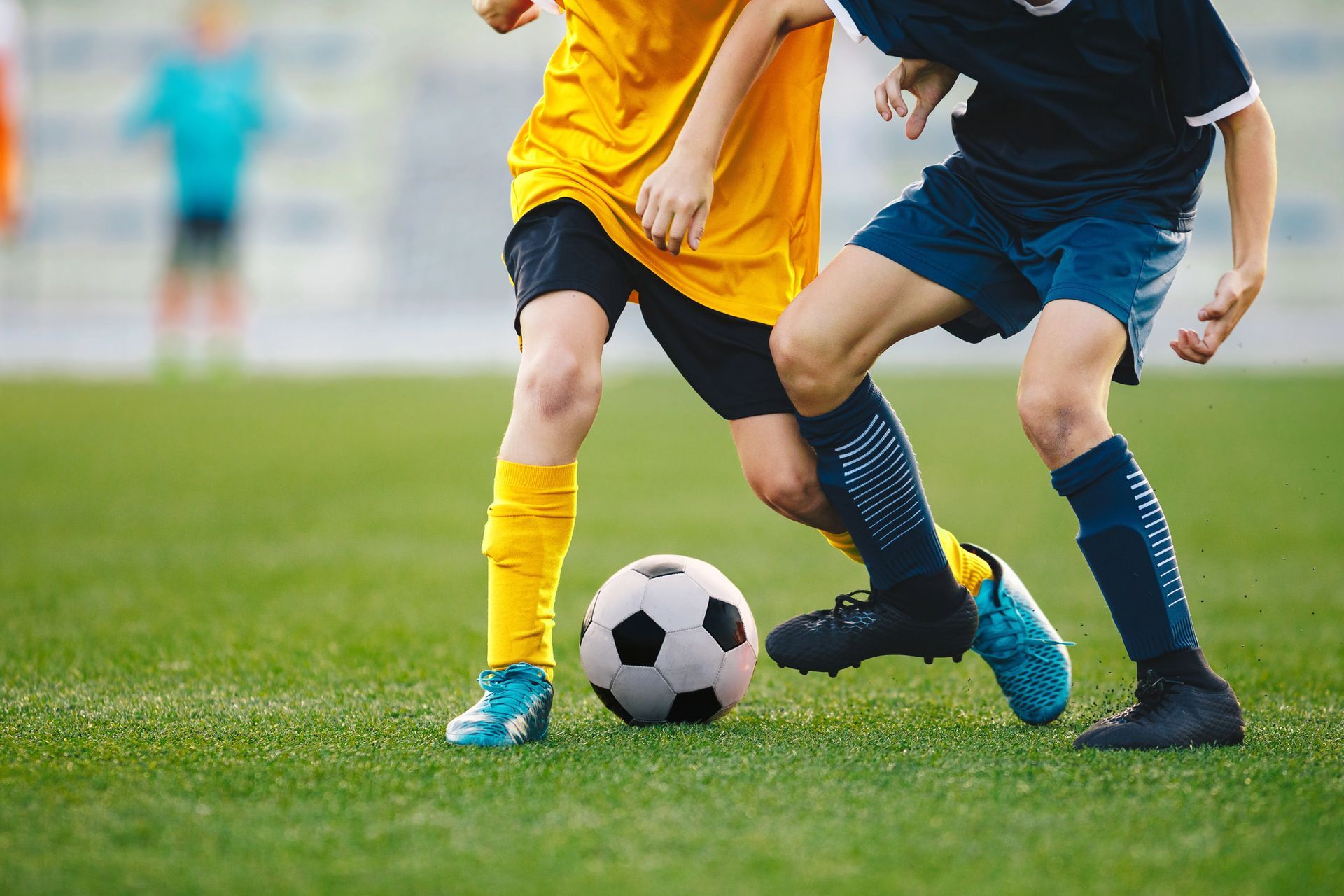 Due calciatori in azione, uno giallo e uno blu, su un campo verde con un pallone da calcio.