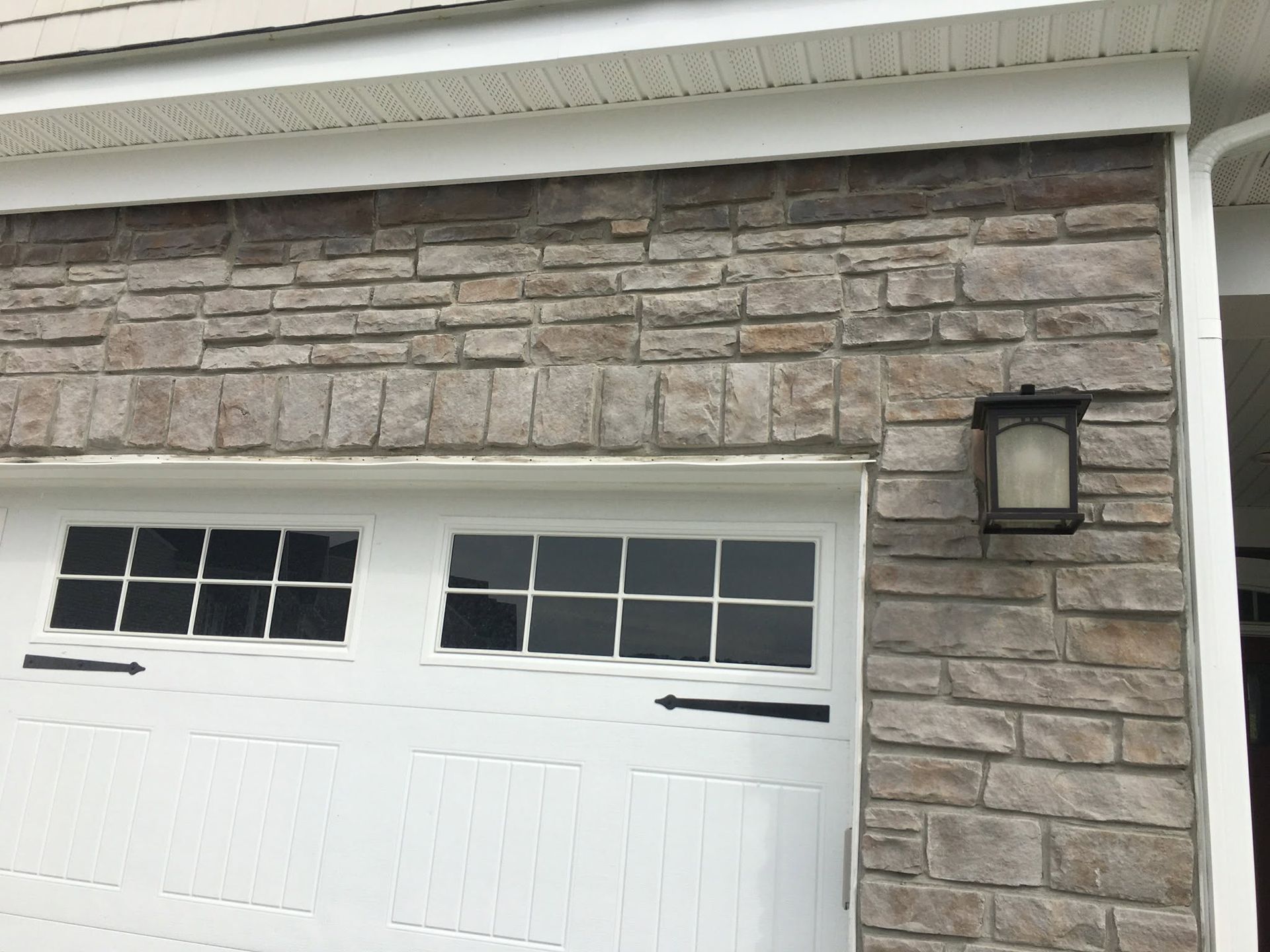 White garage door with small windows beneath a stone exterior wall and porch light