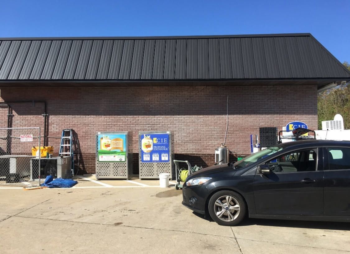Brick storefront with signs out front and a black car parked along the curb.