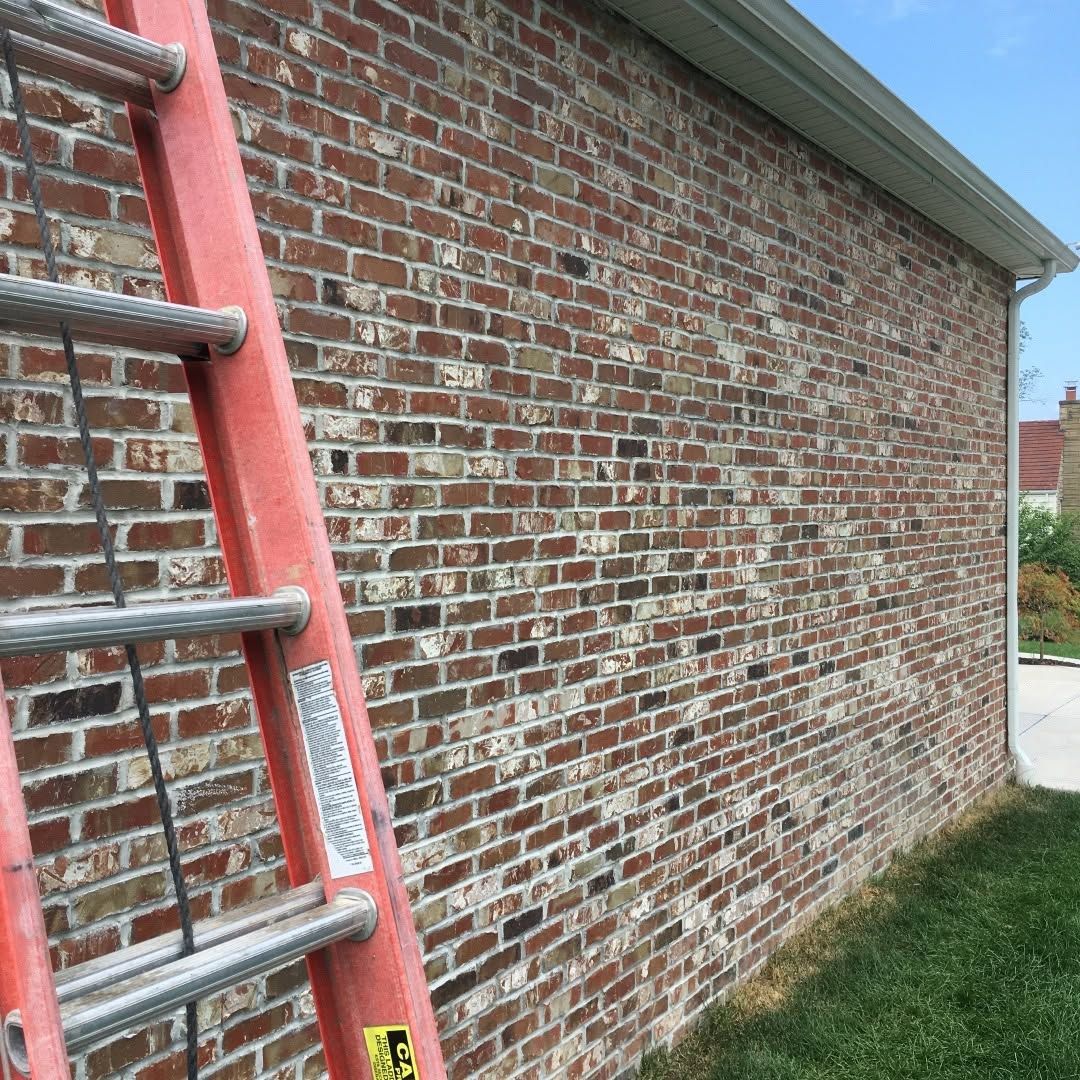 Red ladder leaning against a brick wall beside a grassy yard