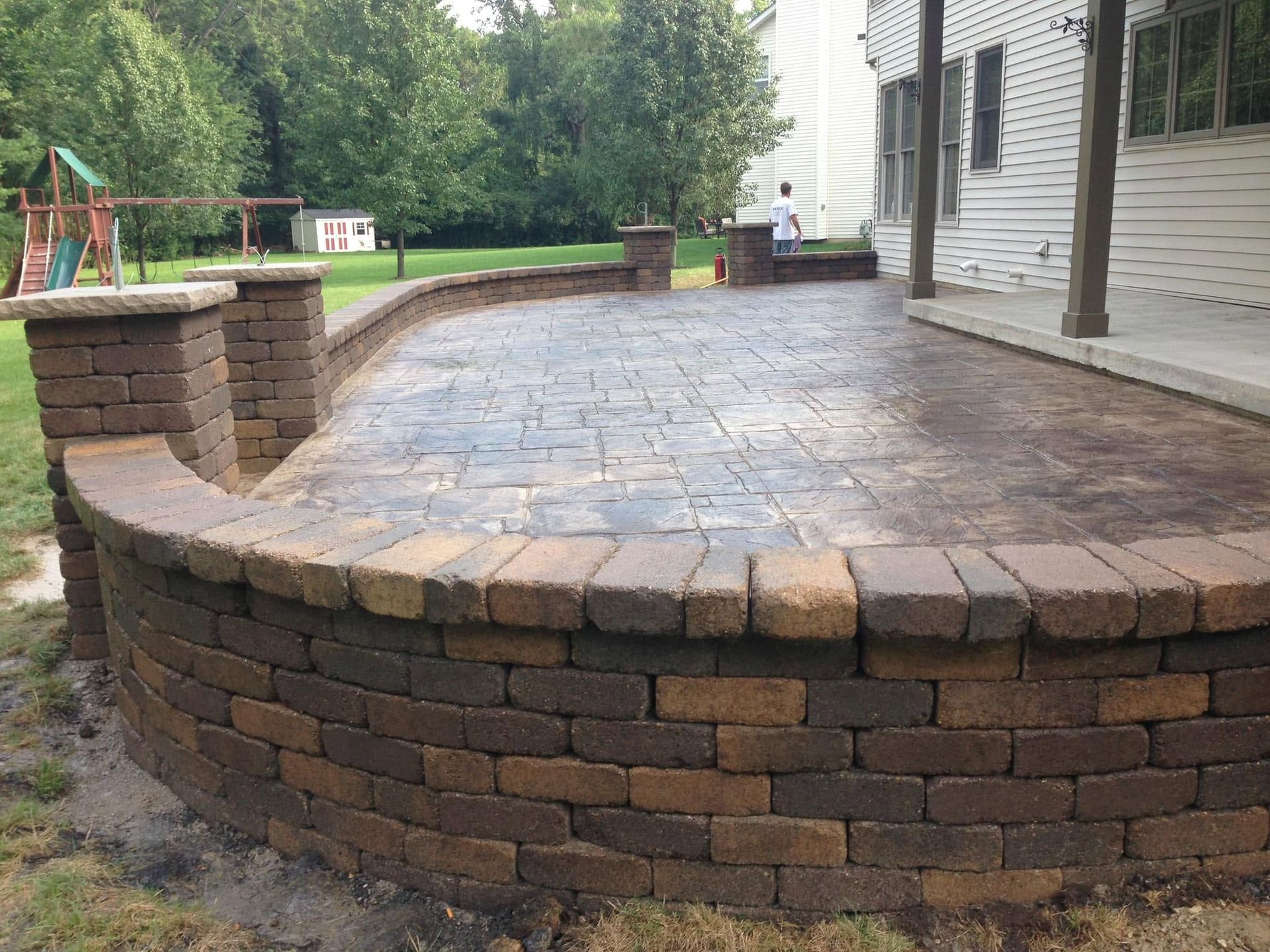 Curved brick patio with stone pavers and a raised retaining wall in a backyard