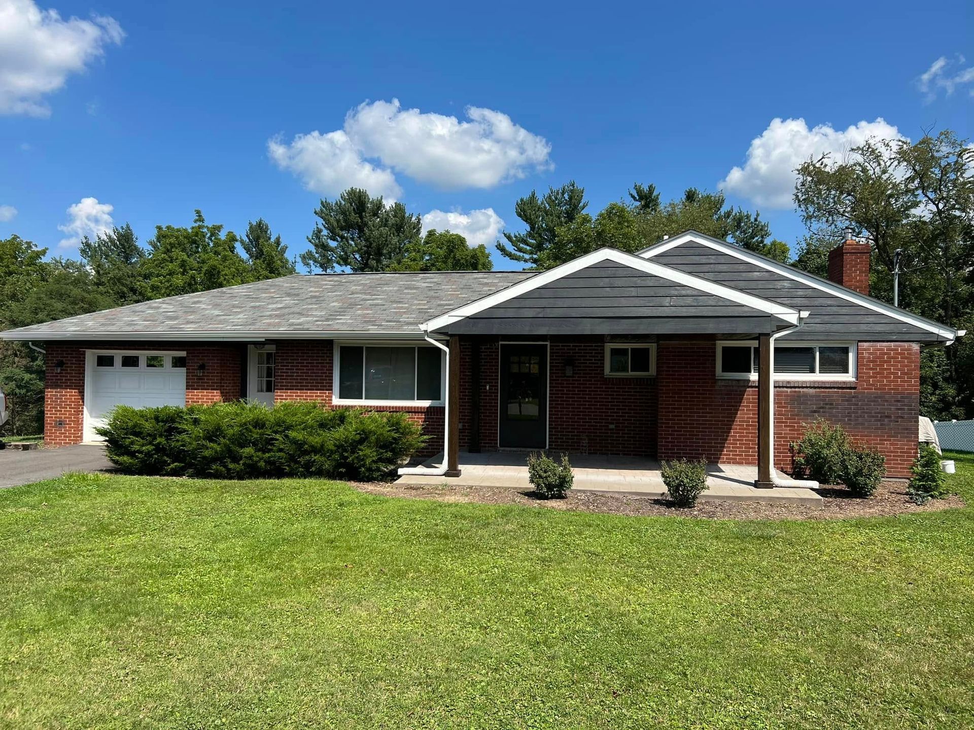 Single-story brick house with white trim, front lawn, and shrubs under a blue sky