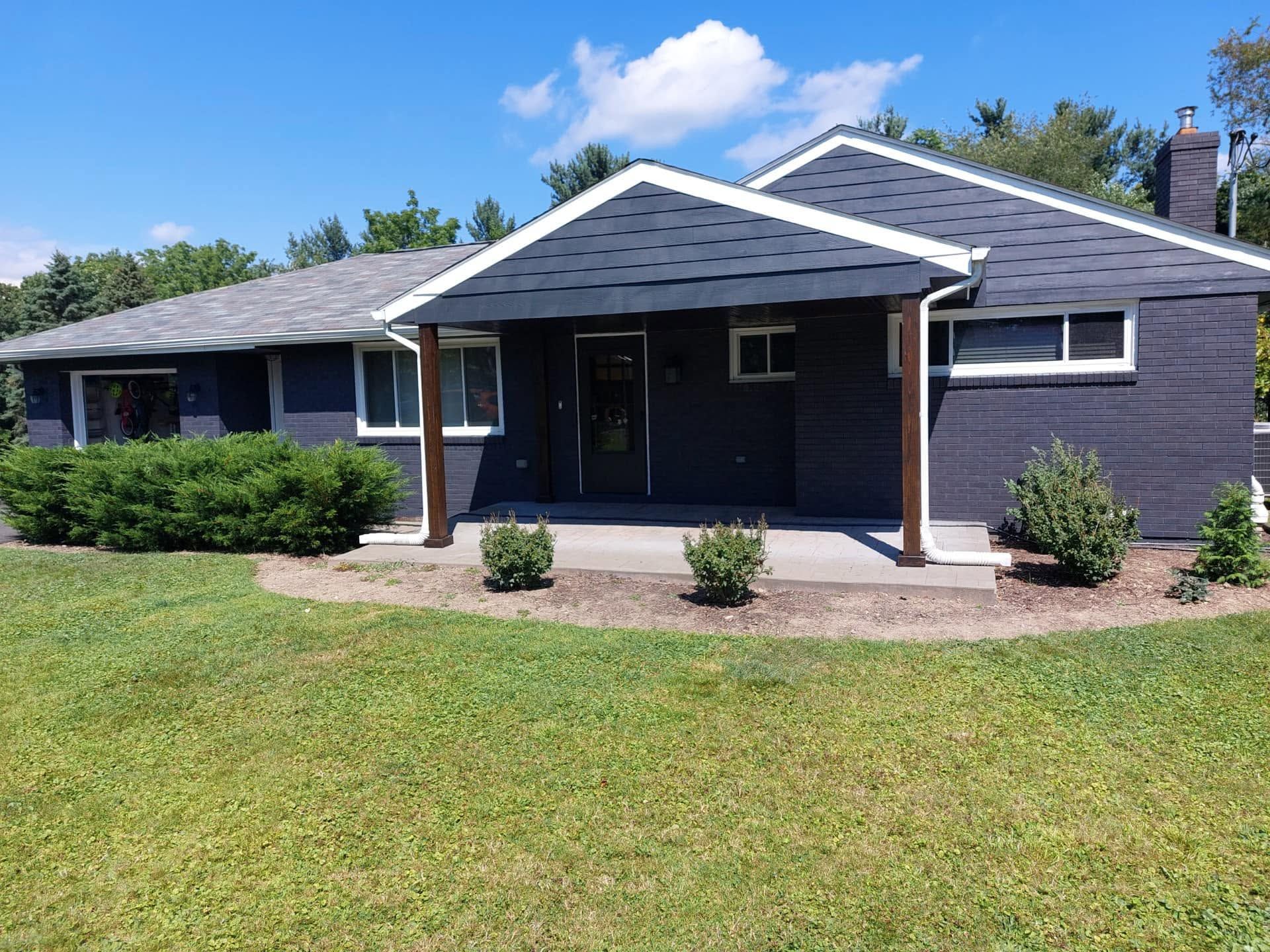 Single-story dark blue house with white trim, front porch, and a grassy lawn under a bright sky