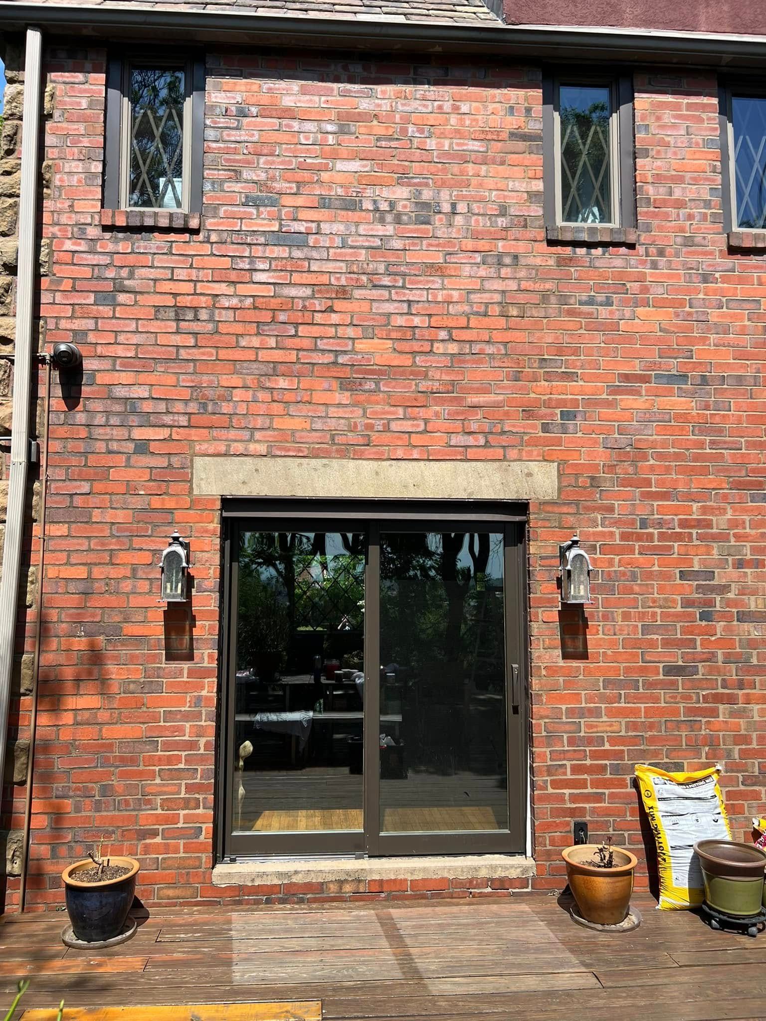 Red brick house exterior with glass patio doors and small windows above a wooden deck