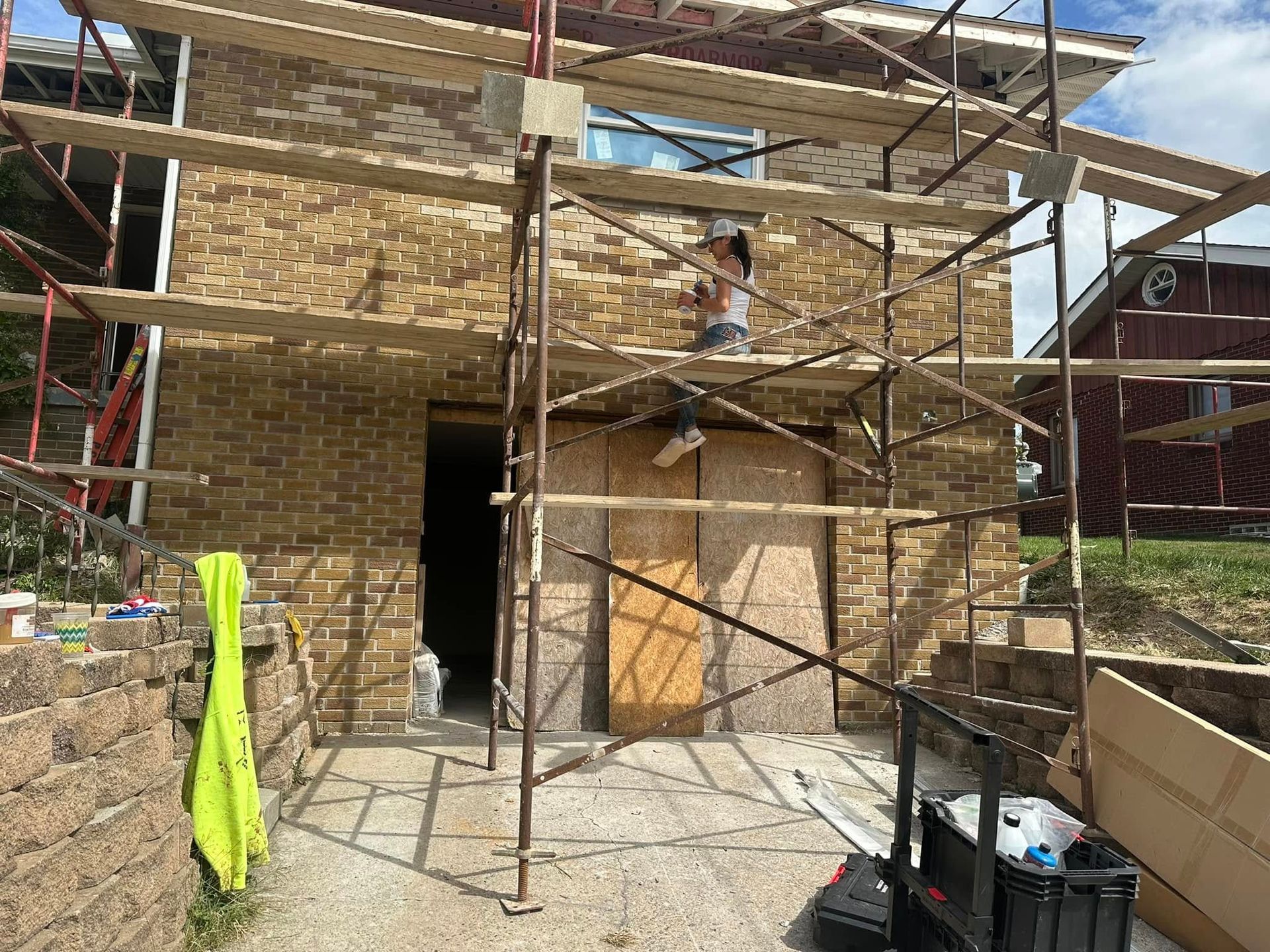 Scaffolding around a brick house under construction, with an open doorway and a bright green cloth hanging nearby
