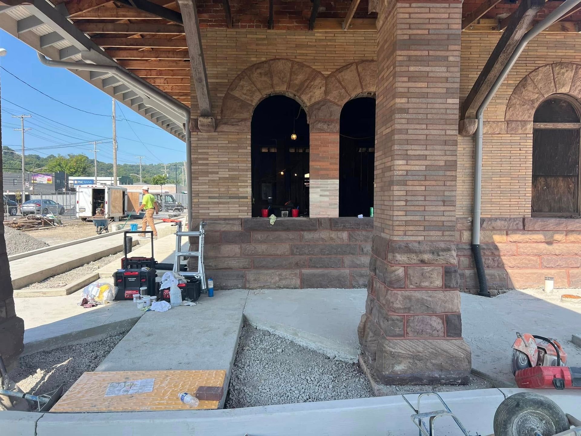 Stone building under construction with arched windows, concrete floor, and tools on the porch