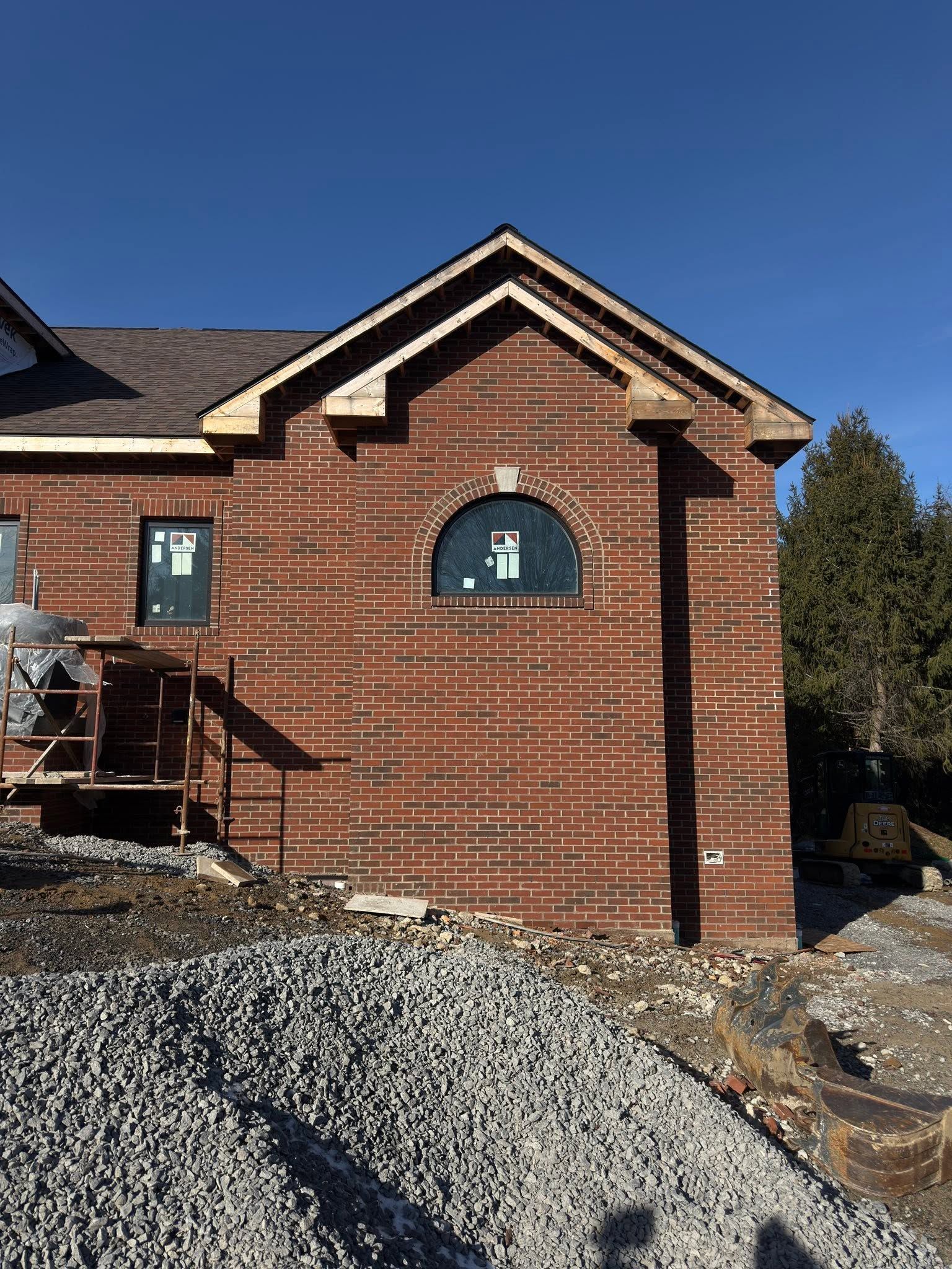 Brick house exterior under construction with a metal scaffold and gravel pile in front.