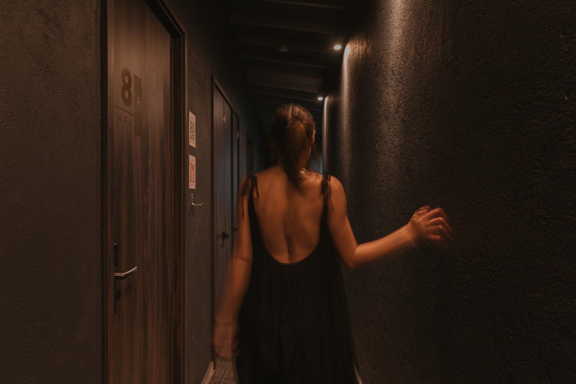 Una mujer con un vestido negro camina por un pasillo oscuro.