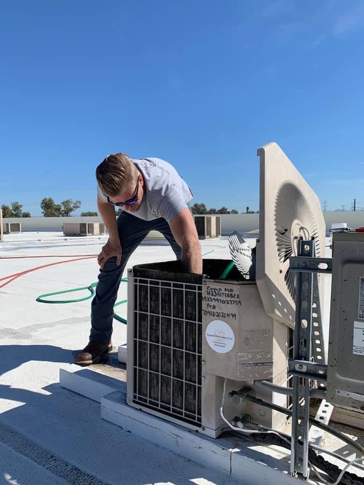 Technician servicing rooftop HVAC unit under a clear blue sky