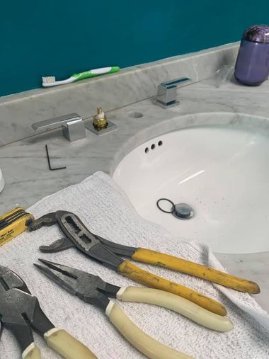 Bathroom sink with pliers and other tools laid on a towel beside the faucet