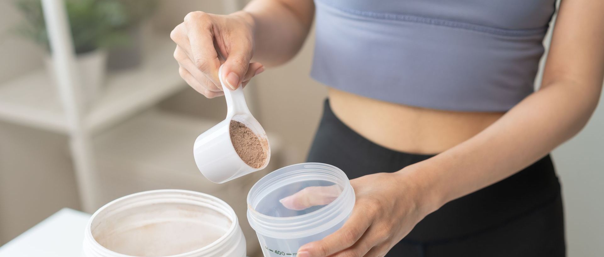 A woman is pouring a scoop of protein powder into a shaker.