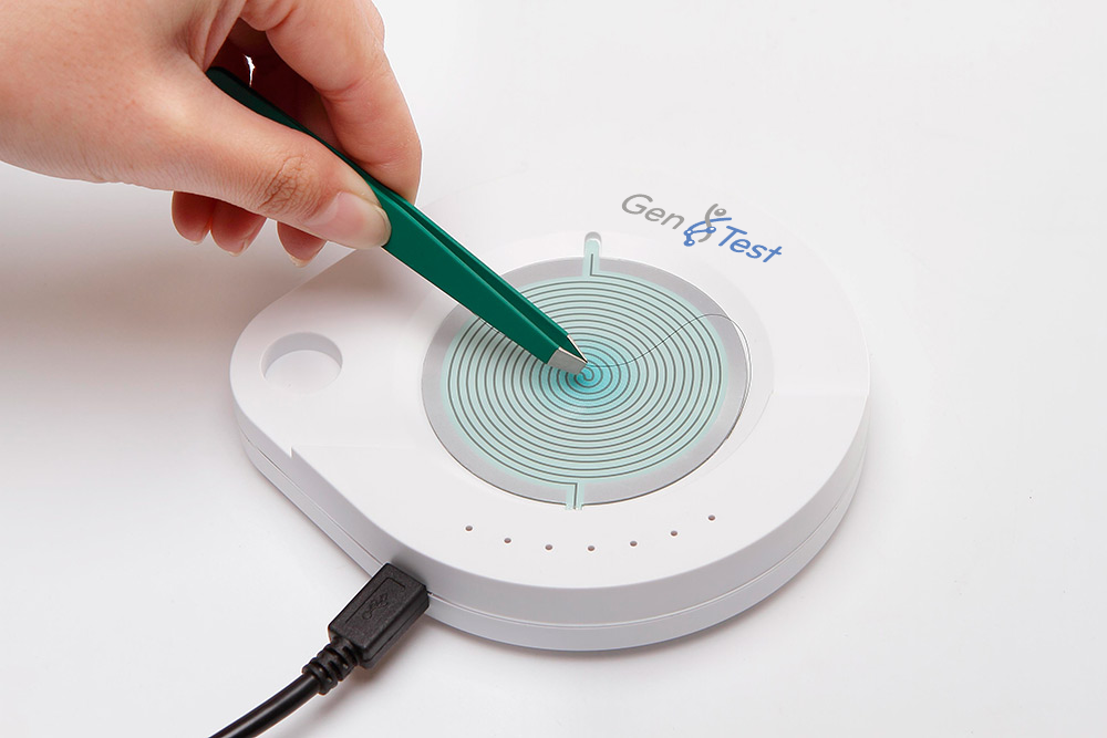 Mano utilizando pinzas sobre un dispositivo blanco con círculos concéntricos para pruebas genéticas.