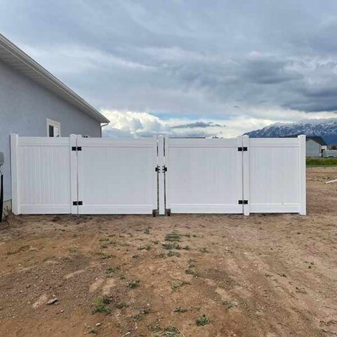 White vinyl double gate/fence beside a house on a dirt yard under a cloudy sky