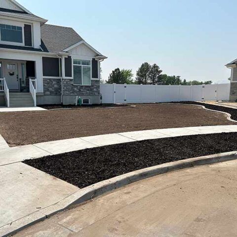 House front yard with fresh landscaping, white fence, and concrete driveway under construction