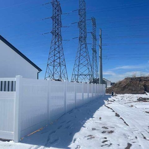 Snowy path beside a white fence, with power lines and metal towers under a clear blue sky.